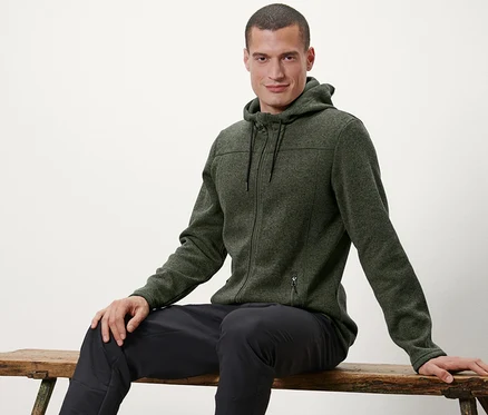 Mann sitzt auf einer Bank und trägt eine Strickfleece-Jacke.