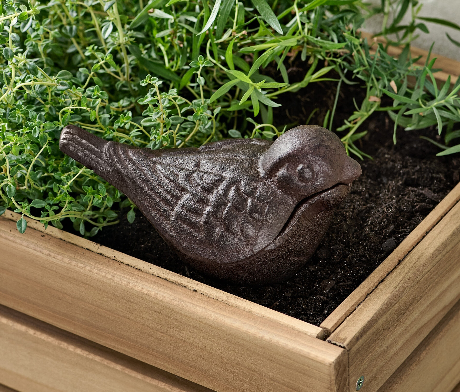 Ein braunes Schlüsselversteck in Vogelform in einem Holzkübel mit Pflanzen.