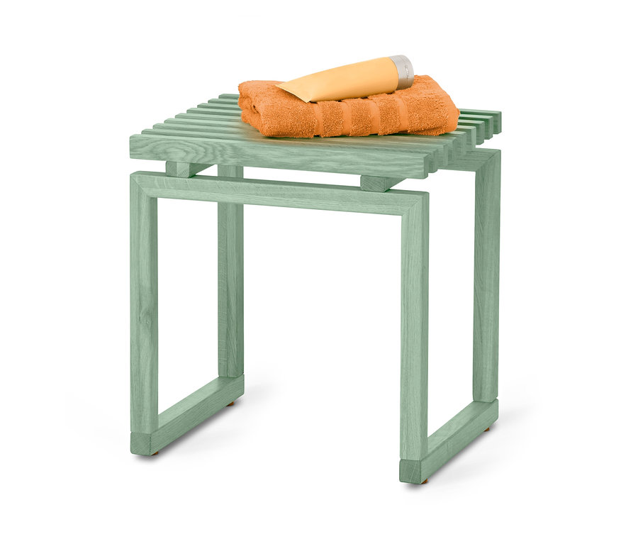 Auf einem salbeifarbenen Massivholzhocker liegen ein oranges Handtuch und eine Tube Hautcreme.
