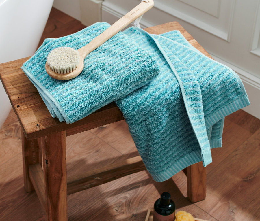 Auf einem Holzhocker liegen zwei aquafarbene Handtücher "2 Handtücher, aqua" und eine Körperbürste.