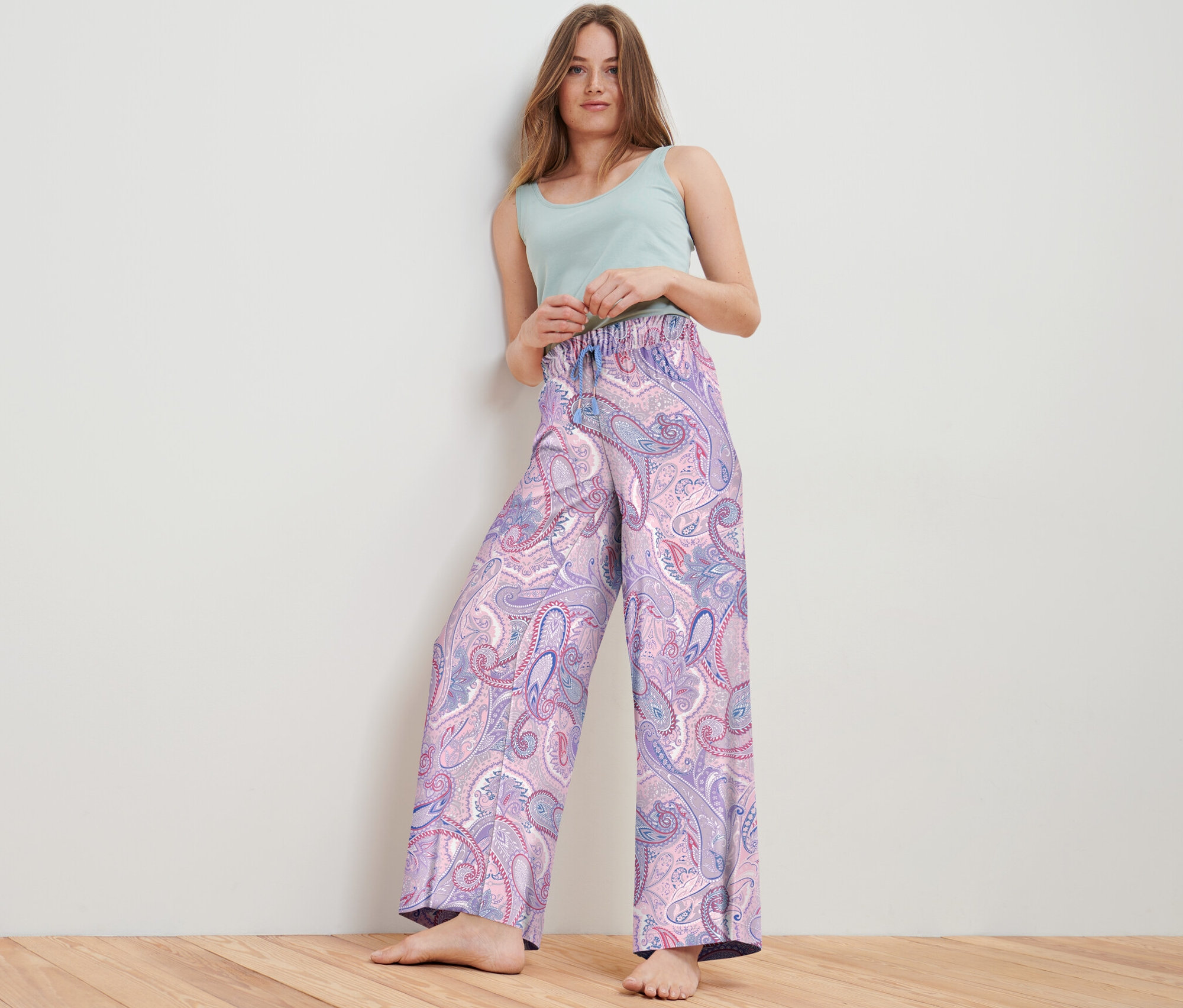 Frau posiert im Studio und trägt eine Web-Relaxhose mit Paisleymuster und ein hellgrünes Top.