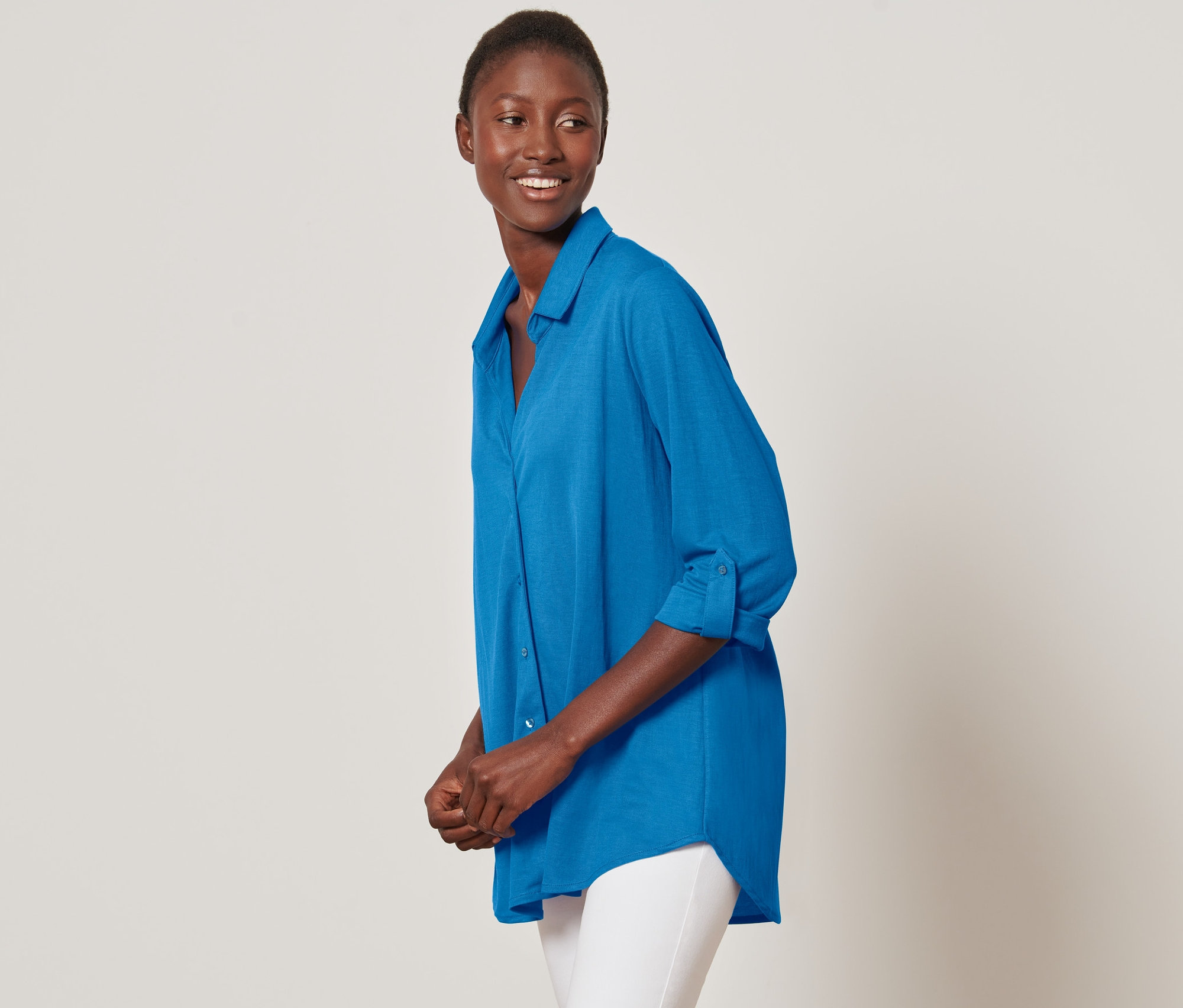 Lächelnde Frau posiert in azurblauer Piqué-Jerseybluse und weißen Hosen.