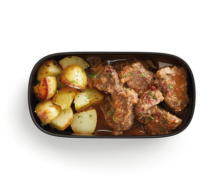Draufsicht auf ein Lunch-Box-Set mit Besteck, das Bratkartoffeln und Fleisch in Sauce enthält.