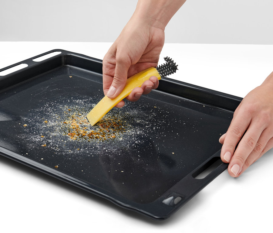 Hände reinigen ein Backblech mit einer Backofenbürste mit Schaber.