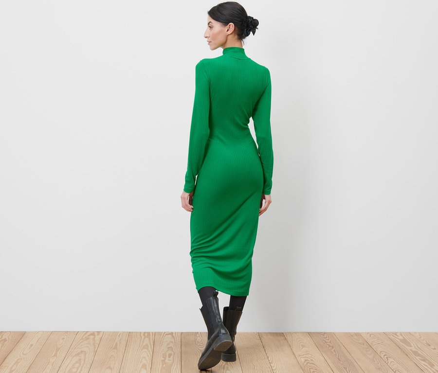 Frau steht mit dem Rücken zur Kamera und trägt ein grünes Jerseykleid und schwarze Stiefel.