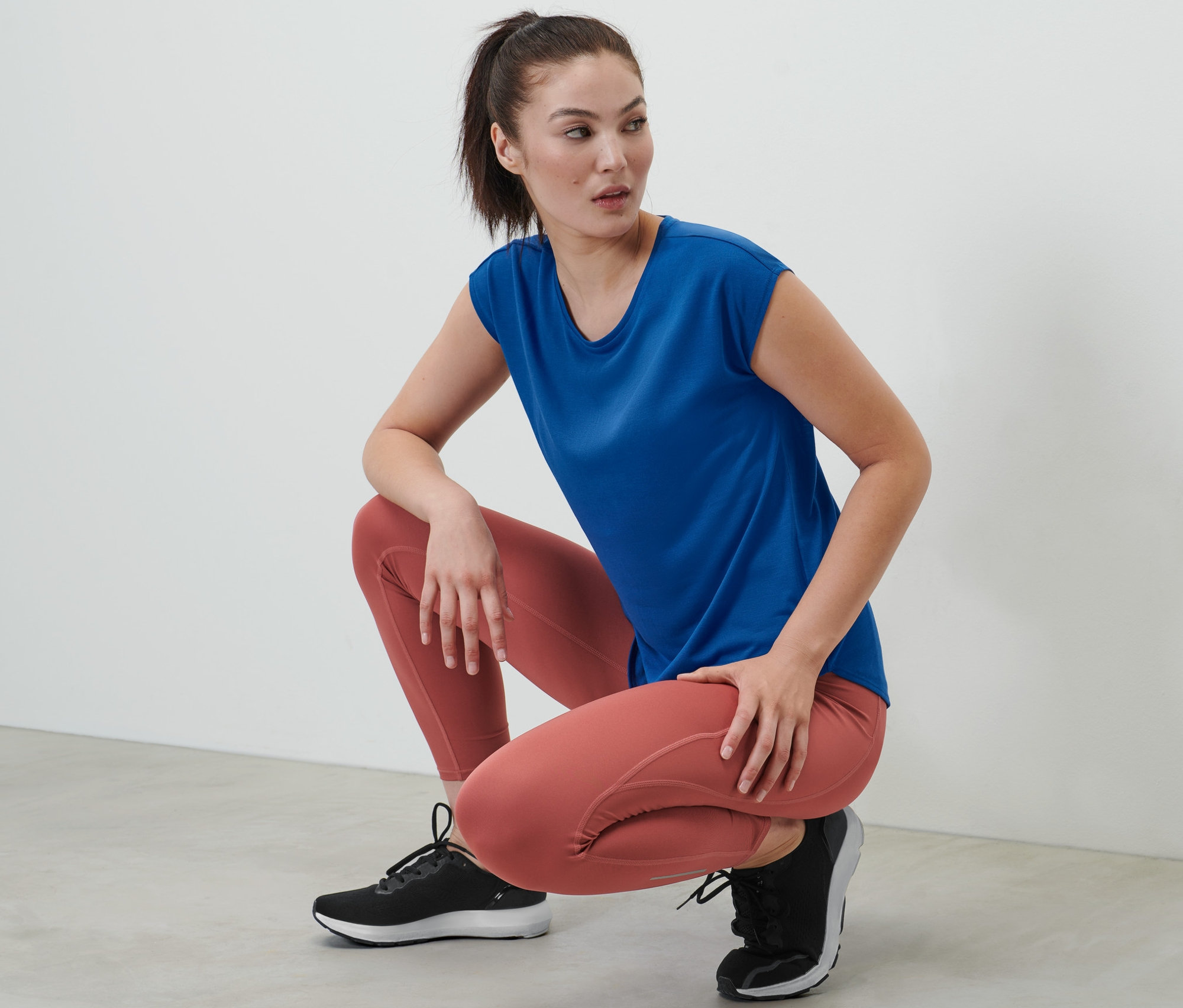 Frau hockt und trägt ein blaues Sportshirt.