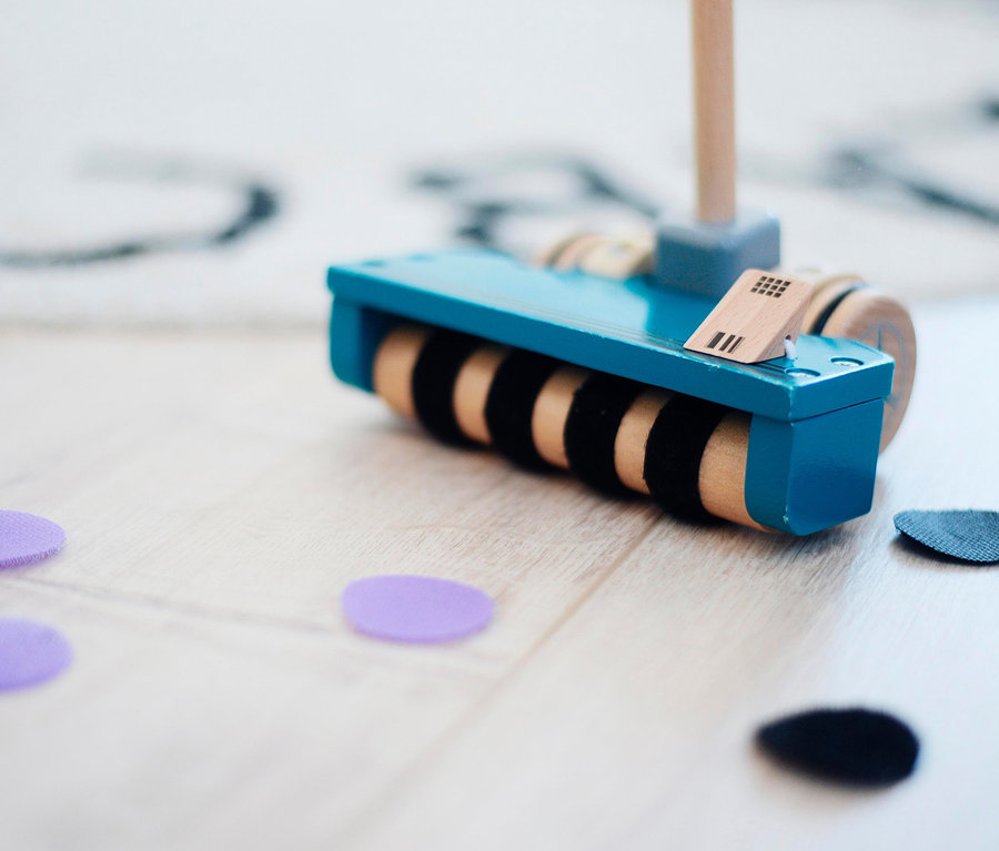 Auf einem Holzboden liegt ein blauer small foot Schiebspielzeug Staubsauger aus Holz und ein paar lila und schwarze Filzkreise.