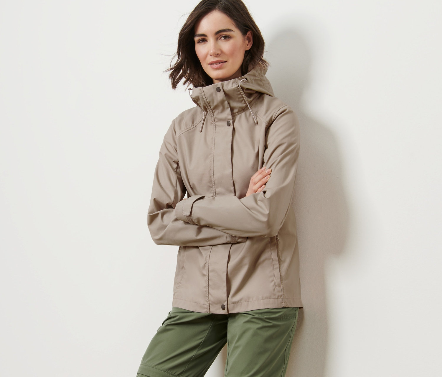 Frau posiert in beiger Allwetterjacke und grüner Hose.