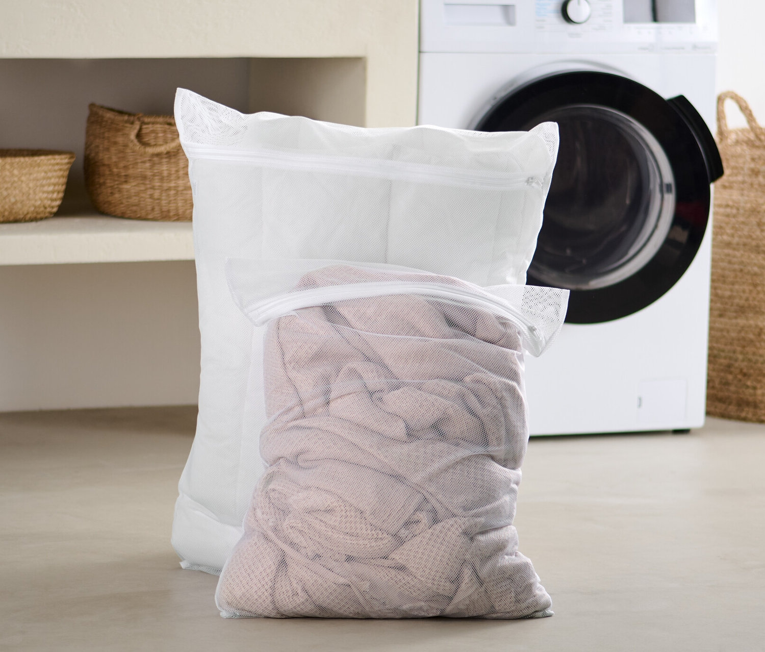 Zwei extragroße Wäschenetze stehen im Badezimmer vor einer Waschmaschine.