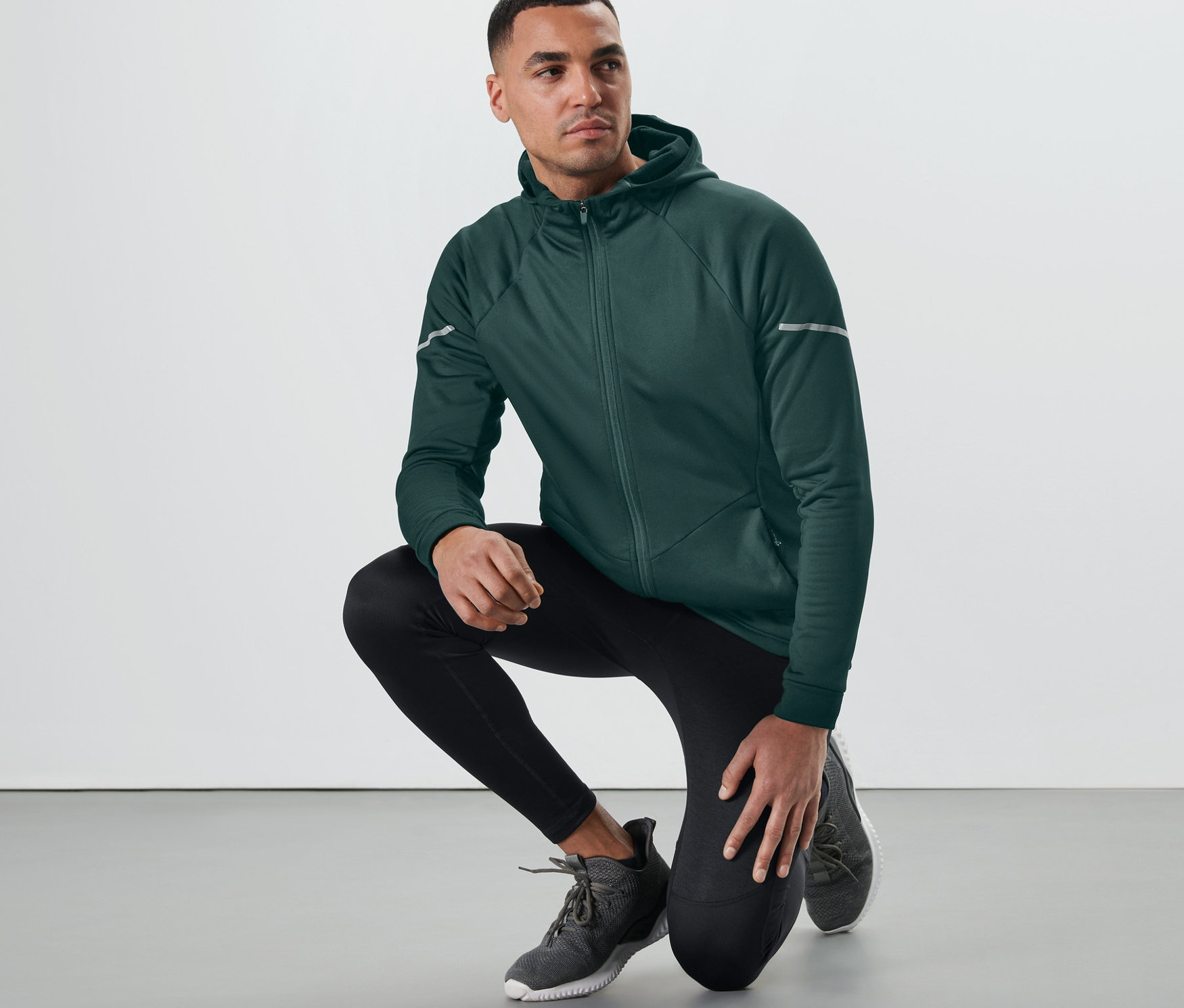 Mann hockt in dunkelgrüner Thermojacke auf dem Boden.