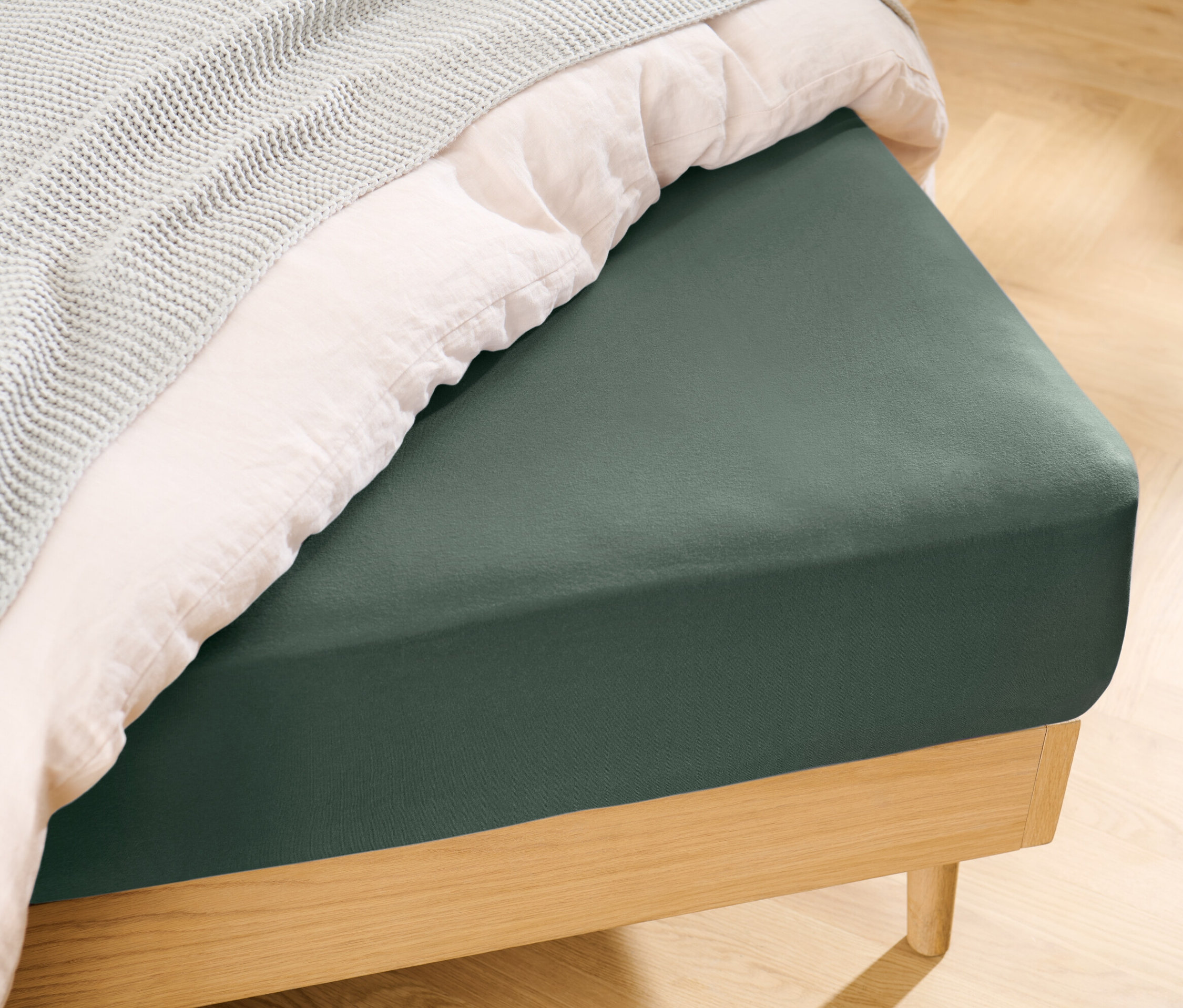 Ein grünes Jersey-Spannbettlaken in Normalgröße liegt auf einem Bett mit einer weißen Decke und einer grauen Tagesdecke.