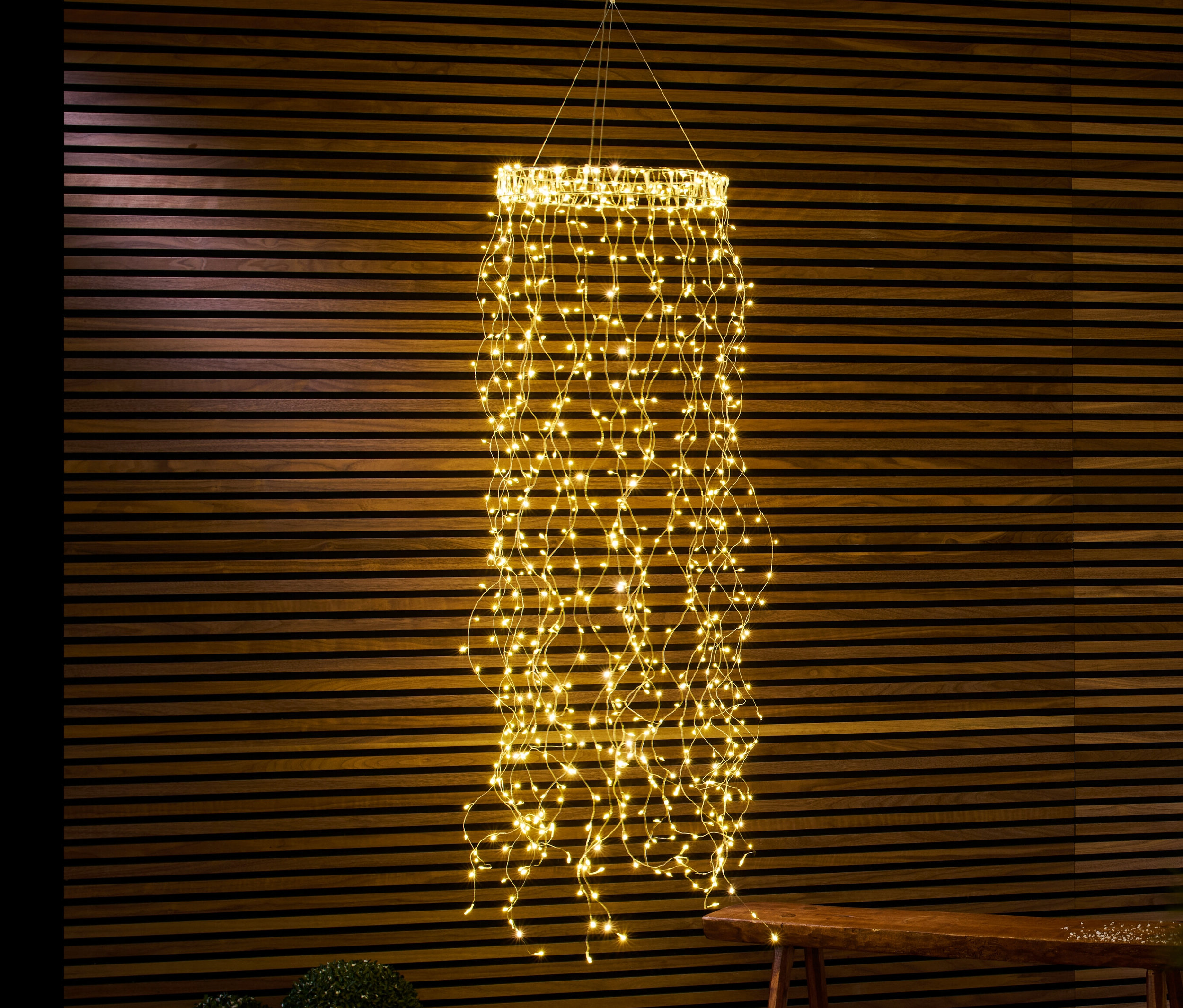 Ein hängender LED-Kranz mit Lichterbündel hängt vor einer Holzwand.