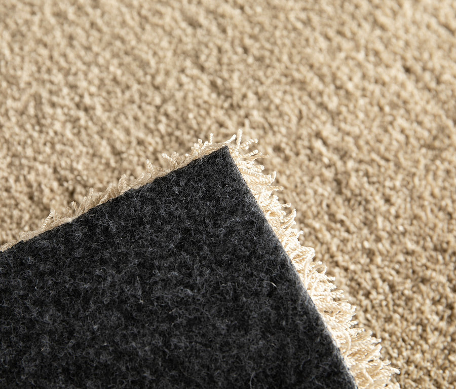 Detailansicht einer Ecke des beigen Teppichs "Mellow" mit schwarzer Unterseite.