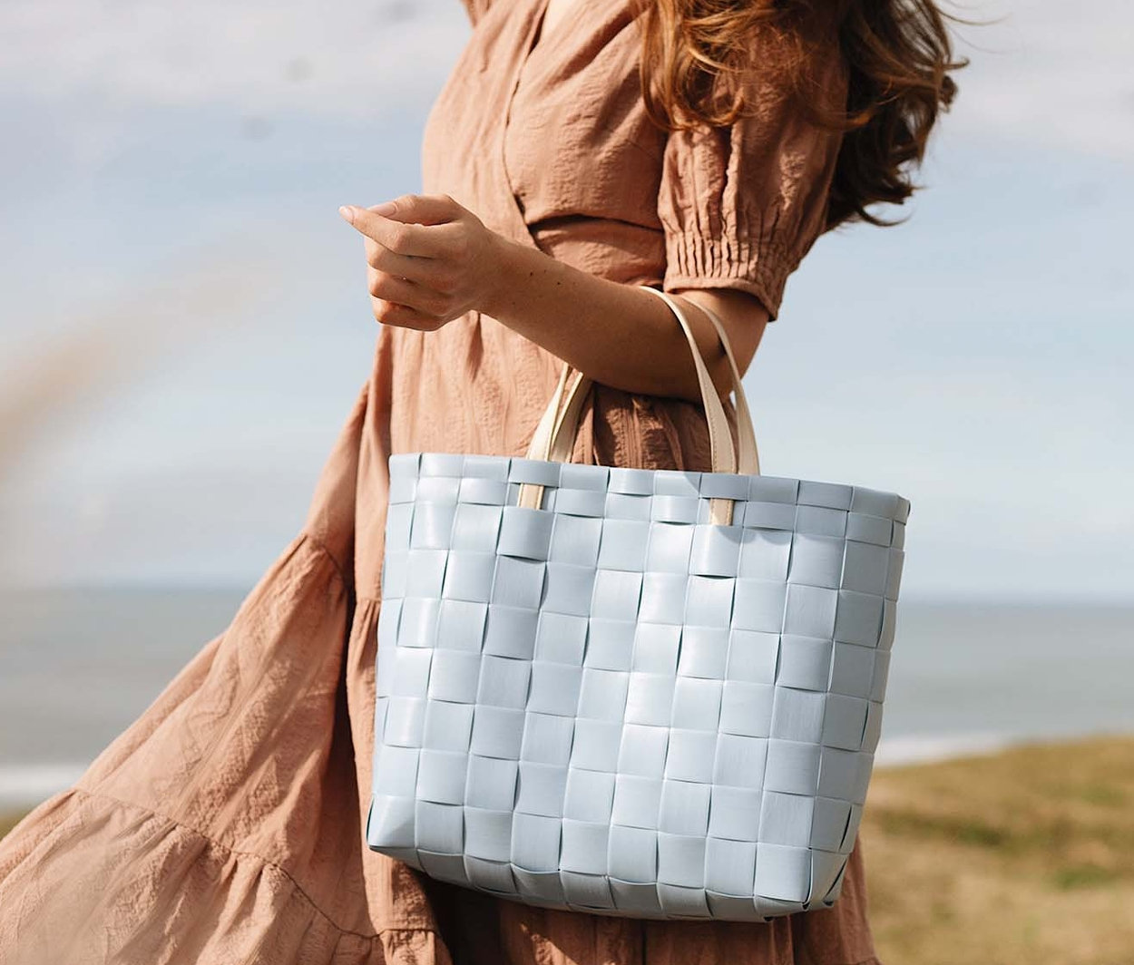 Frau geht am Strand entlang und hält eine hellblaue Handed By Shopper-Tasche »Petite«.