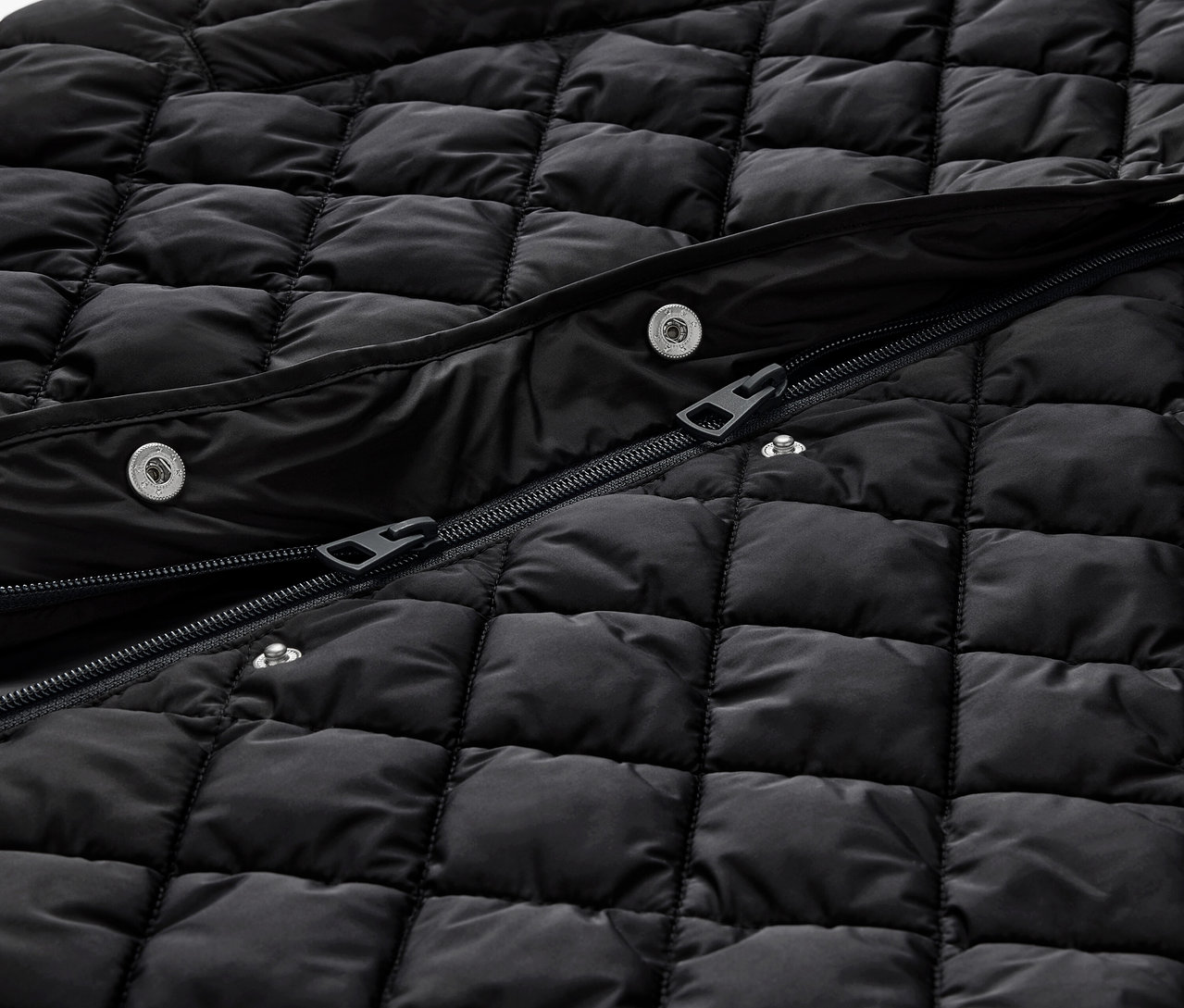 Detail einer langen schwarzen Steppweste mit Kapuze, mit Reissverschluss und Druckknöpfen.