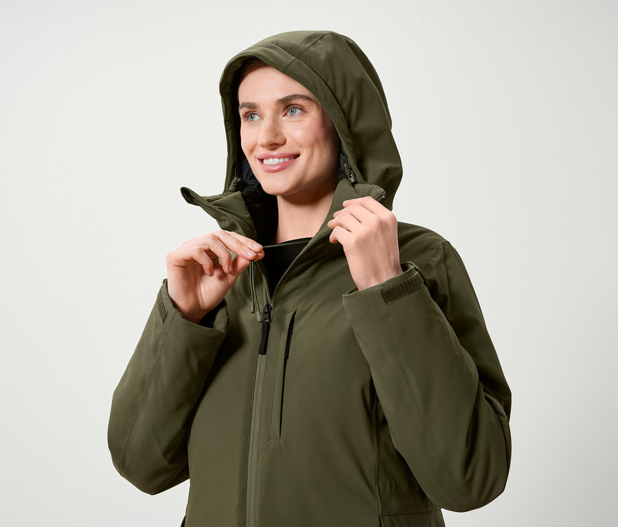 Frau reguliert die Kapuze einer olivgrünen Jacke.