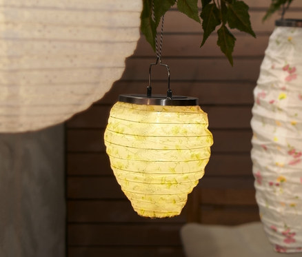 Drei kleine Solar-Lampions hängen an einem Baum über einem Tisch und einer Bank.