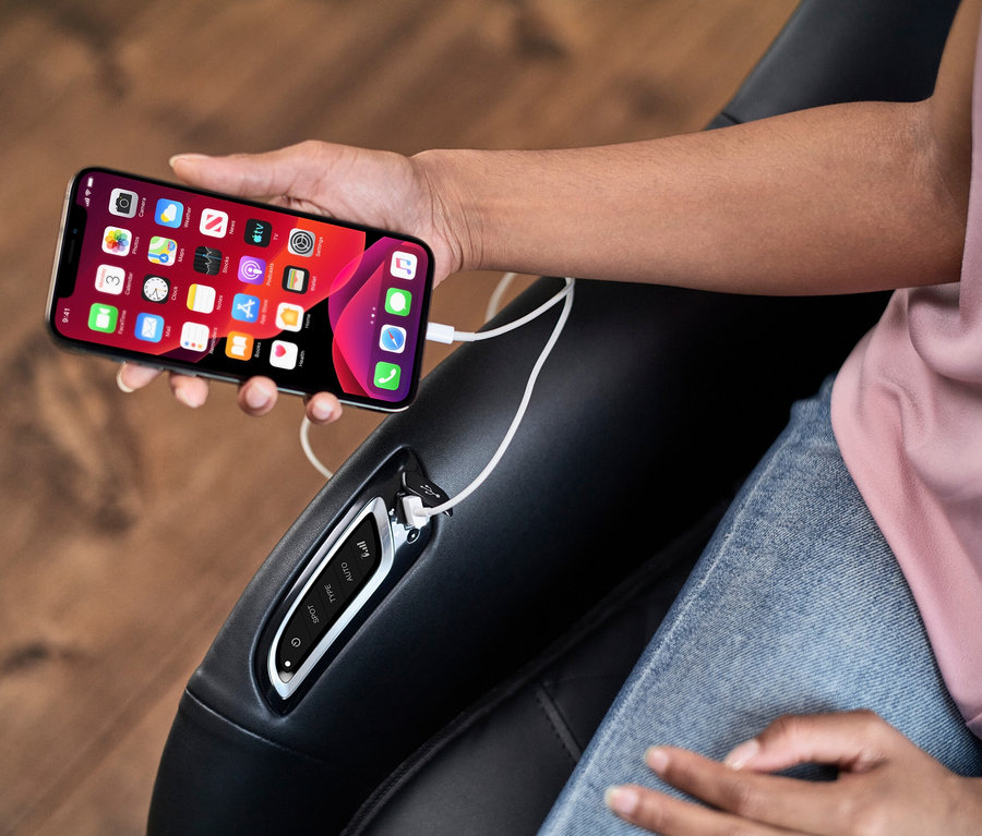 Frau hält ein aufladendes Smartphone in der Hand, während sie in einem Medisana Massagesessel »RS 660« sitzt.