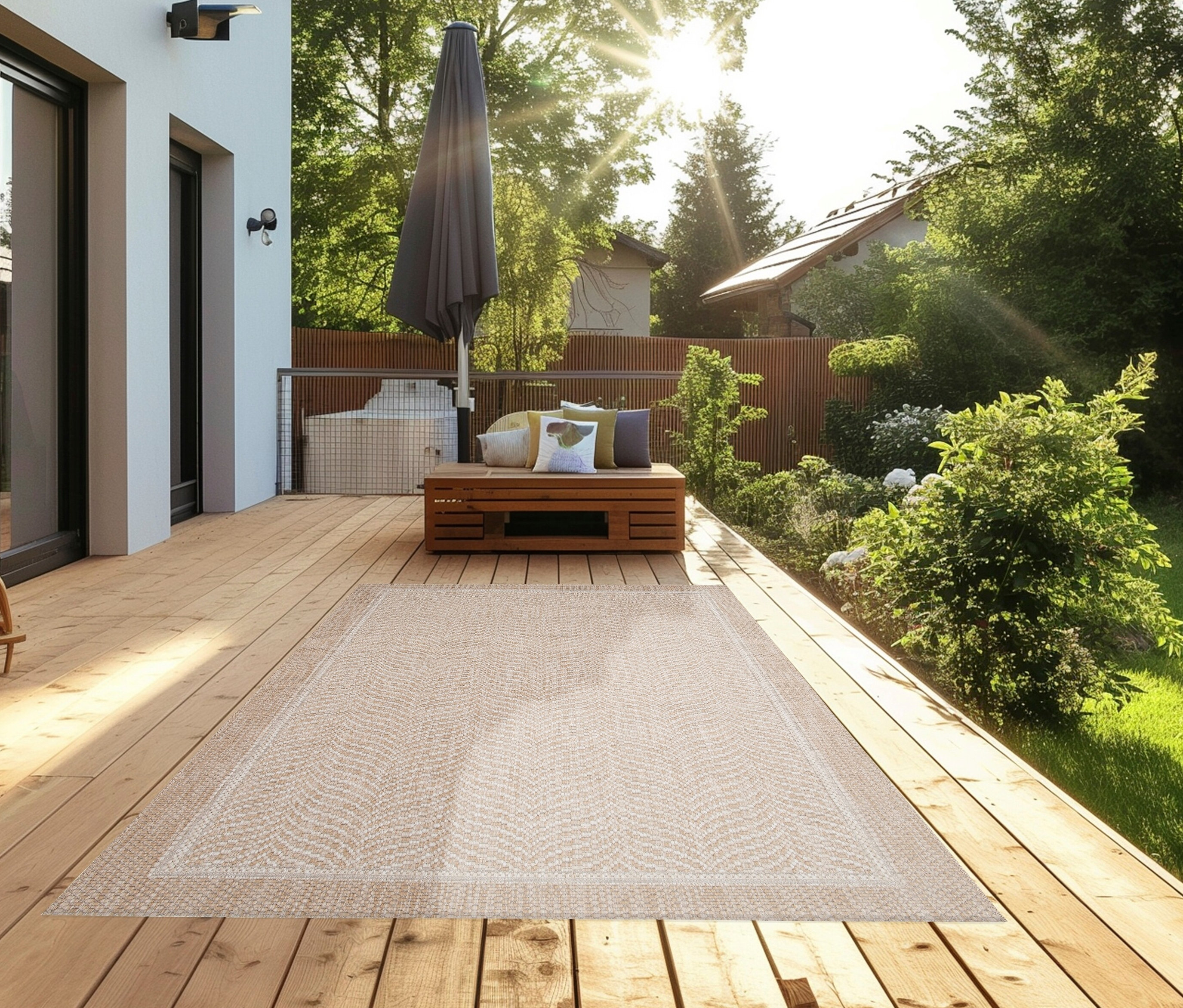 Ein beiger Teppich »Twine« mit Fischgrätenmuster liegt auf einer Holzterrasse neben einer Sitzecke.