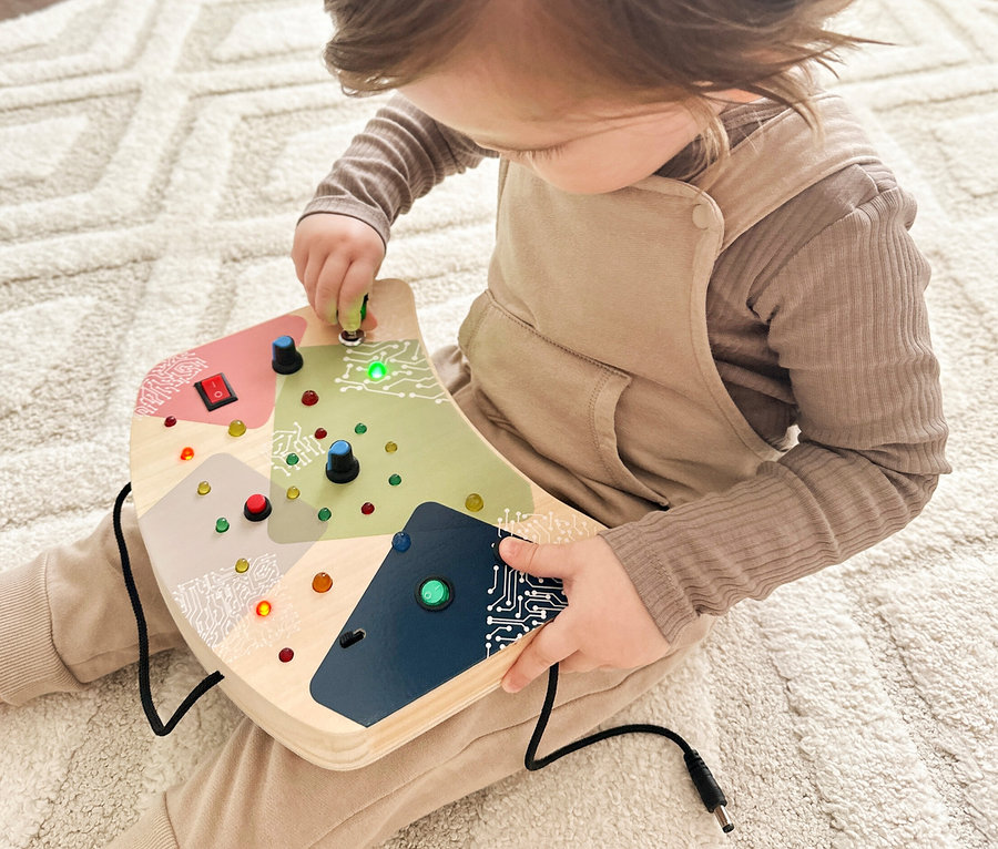 Kleinkind sitzt auf Teppich und spielt mit small foot Motorikbrett, LED und Schalter.