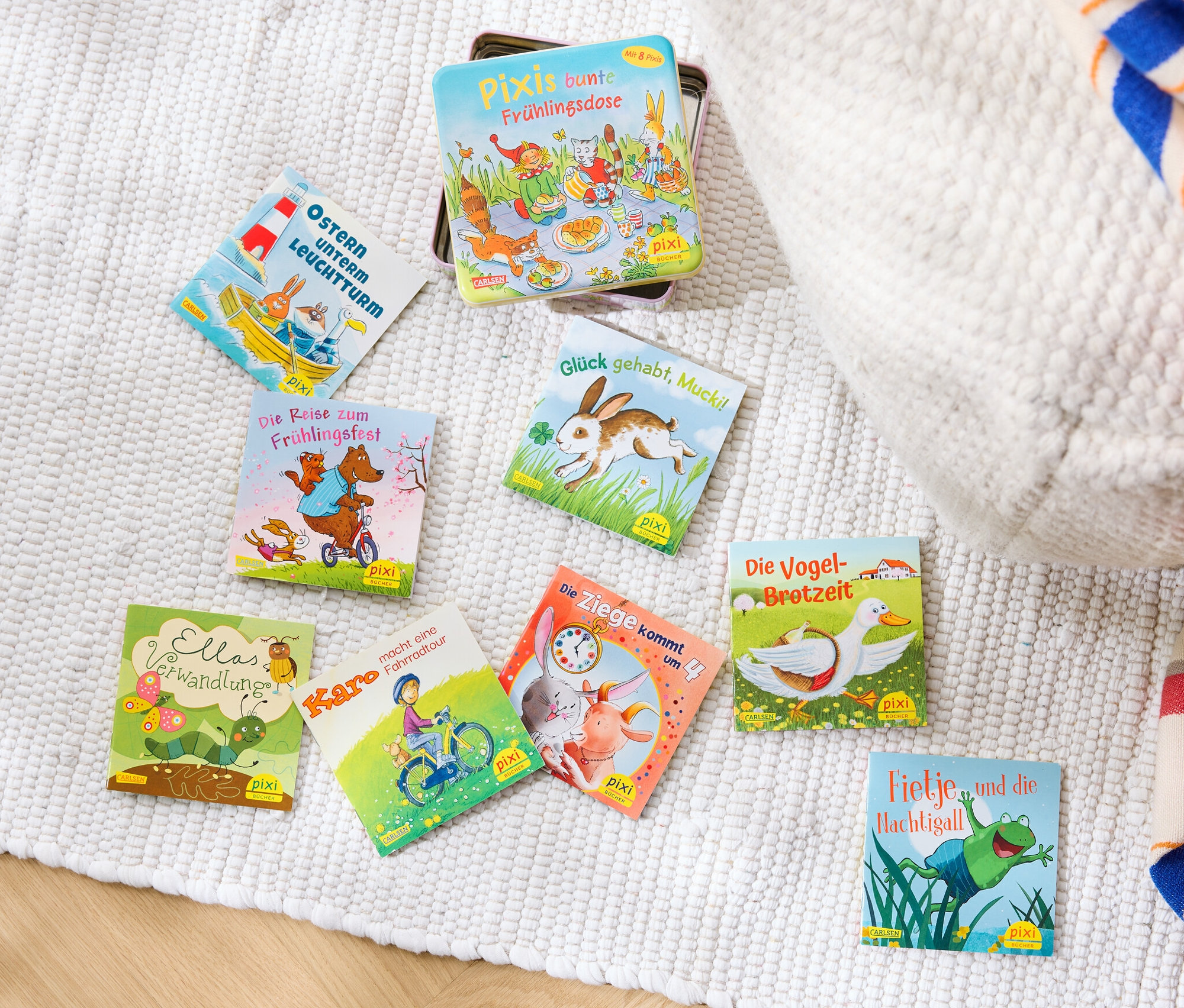 Auf einem weißen Teppich liegt ein Bücher-Set »Pixis bunte Frühlingsdose« und ein paar andere Bücher.