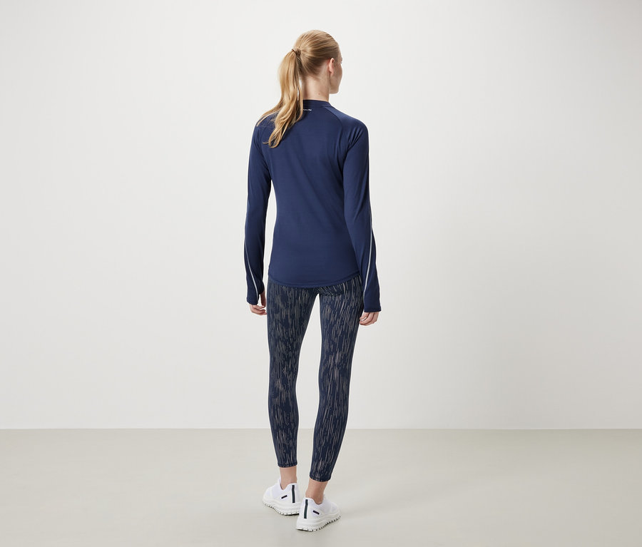 Frau in marineblauem Sportlangarmshirt und gemusterten Leggings steht mit dem Rücken.