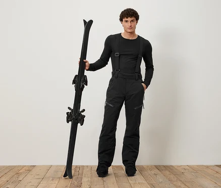 Mann in schwarzer Skibekleidung hält schwarze Skier.