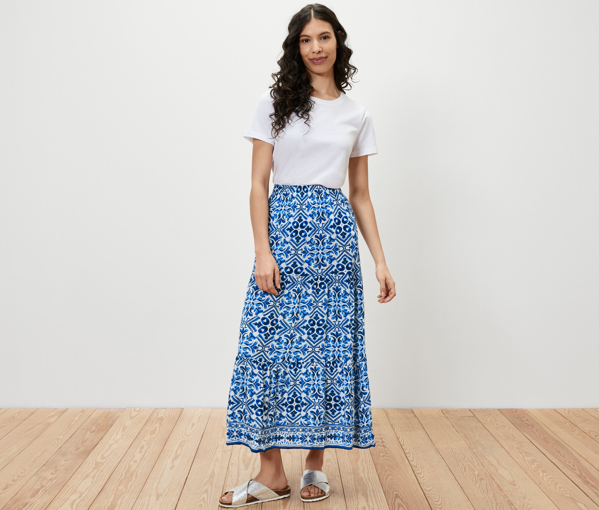 Frau steht und trägt ein weißes T-Shirt und einen bedruckten Webrock.