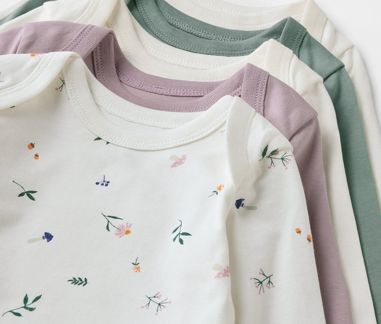 Detailaufnahme von fünf Baby-Bodys mit Mitwachsfunktion in Weiß, Rosa und Grün.