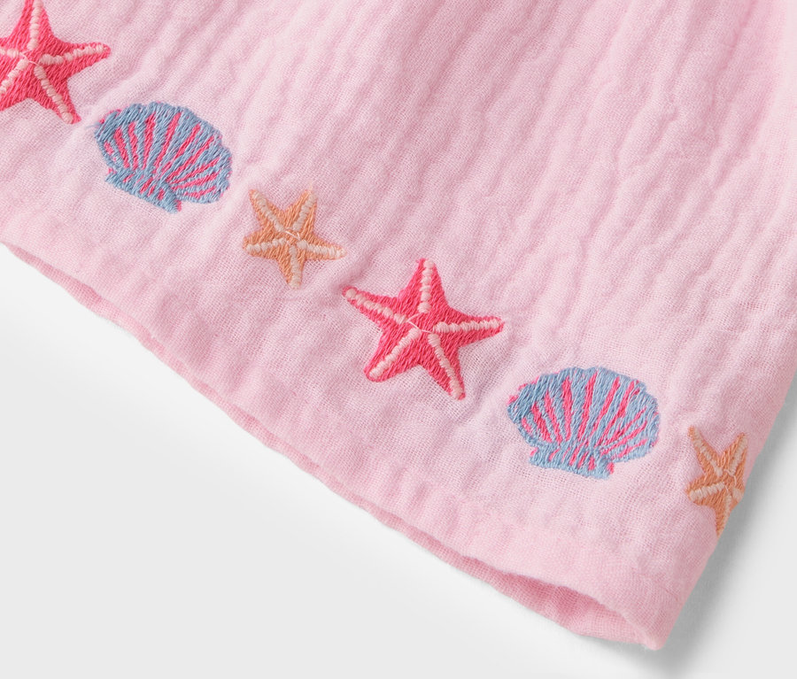 Nahaufnahme eines rosa Stoffes mit aufgestickten rosa Seesternen und blauen Muscheln.