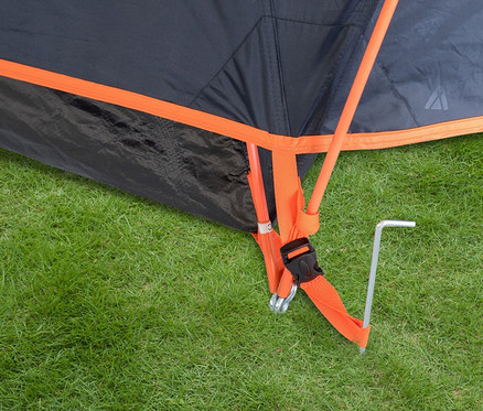 Detailaufnahme eines Tambu »HAIKA 2« 2-Personen-Kuppelzelts auf einer Wiese, befestigt mit Heringen und orangefarbenen Spanngurten.