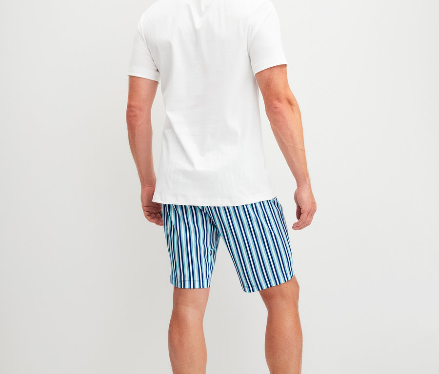Rückansicht eines Mannes mit rotem Haar, der ein weißes T-Shirt und blau-weiß gestreifte Shorts trägt.