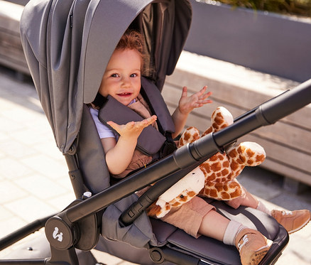 Kleines Kind sitzt in einem grauen Kinderwagen mit einem Giraffenspielzeug.
