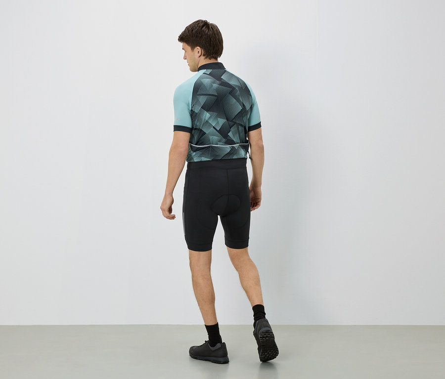Mann von hinten in Radsportbekleidung, Trikot hellblau mit geometrischem Muster, schwarze Hose, schwarze Socken und Schuhe.