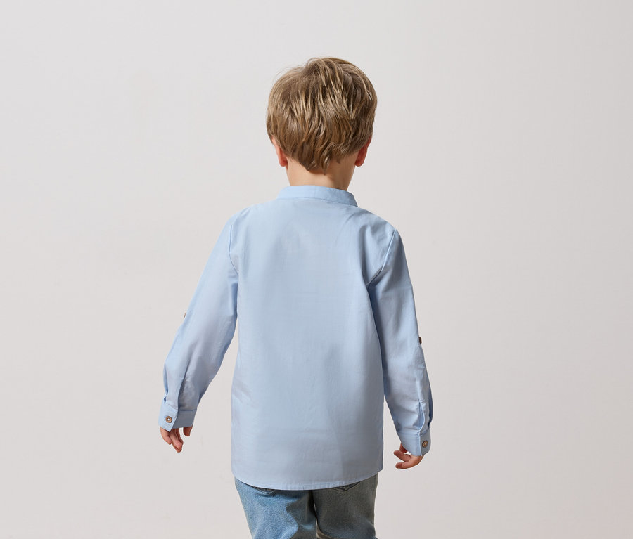 Rückansicht eines Kindes mit blonden Haaren, das ein hellblaues Hemd und Jeans trägt.