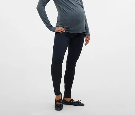 Schwangere mit grauem Oberteil und MAMALICIOUS 2er Pack Leggins »MLEMMA« posiert mit Hand auf der Hüfte vor einem weißen Hintergrund.