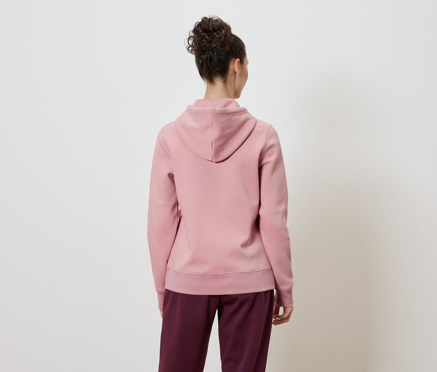 Rückansicht einer Frau mit Duttfrisur, die einen rosafarbenen Kapuzenpullover und weinrote Hosen vor einem weißen Hintergrund trägt.