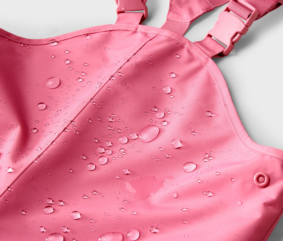 Nahaufnahme einer pinkfarbenen Regenhose mit Trägern und Wassertropfen auf dem Stoff.
