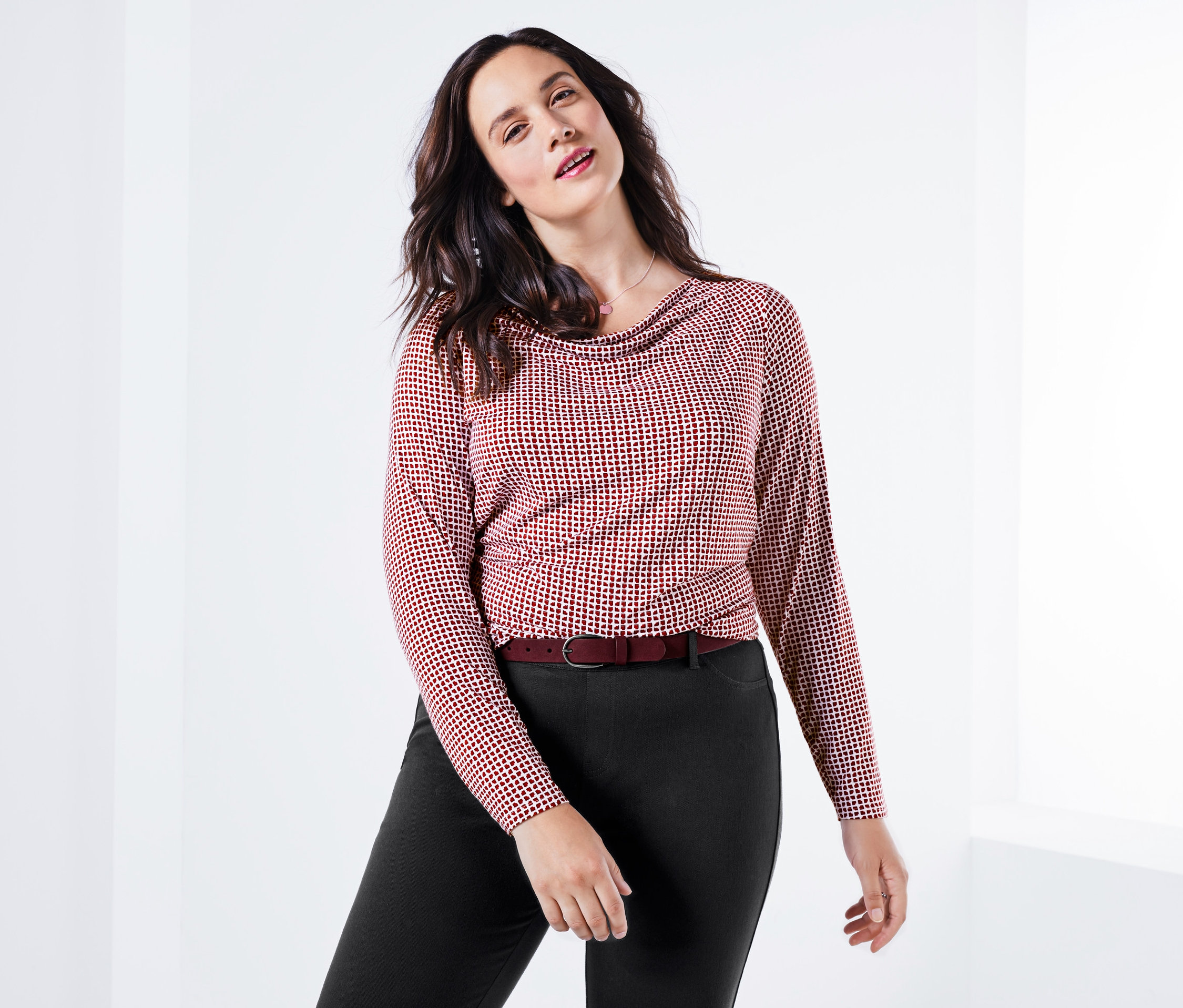 Frau posiert in Shirt mit Wasserfall-Ausschnitt, Jeggings und Gürtel.