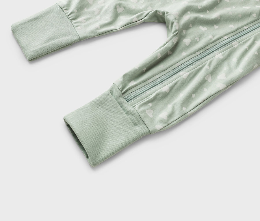 Nahaufnahme eines hellgrünen Baby-Schlafanzugs mit weißem Herzmuster und einem durchgehenden Reißverschluss.