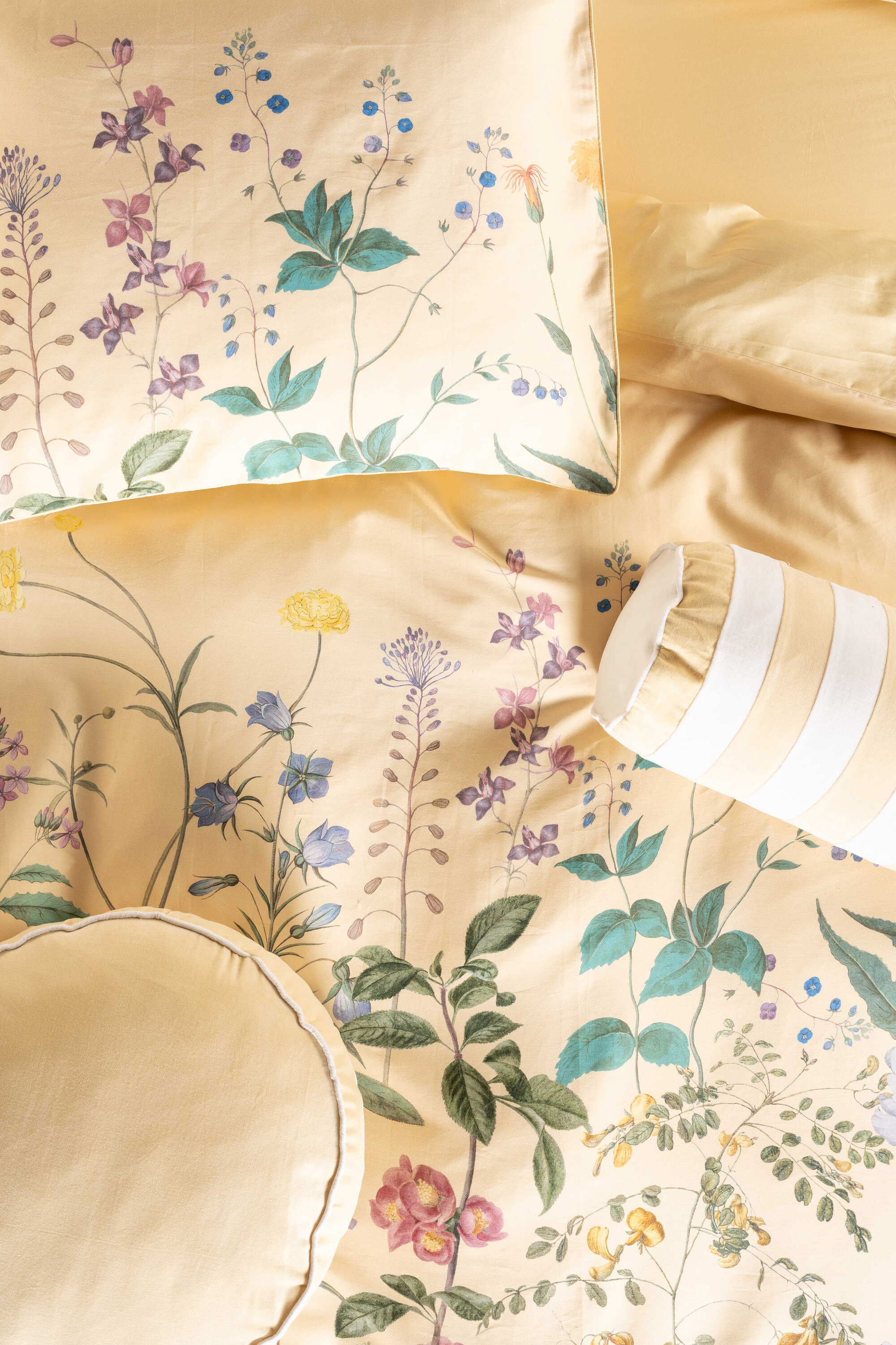 Nahaufnahme von gelber Bettwäsche mit floralem Muster, bestehend aus Kissen und Bezügen.