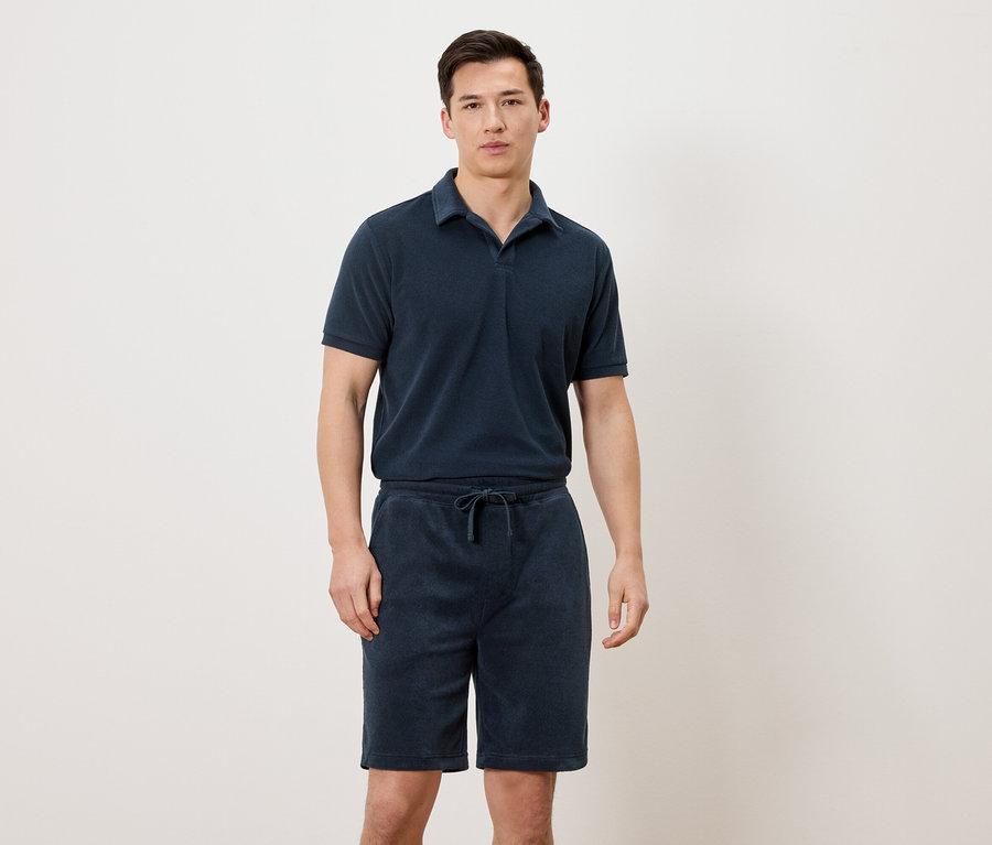 Mann trägt ein marineblaues Poloshirt und marineblaue Shorts.
