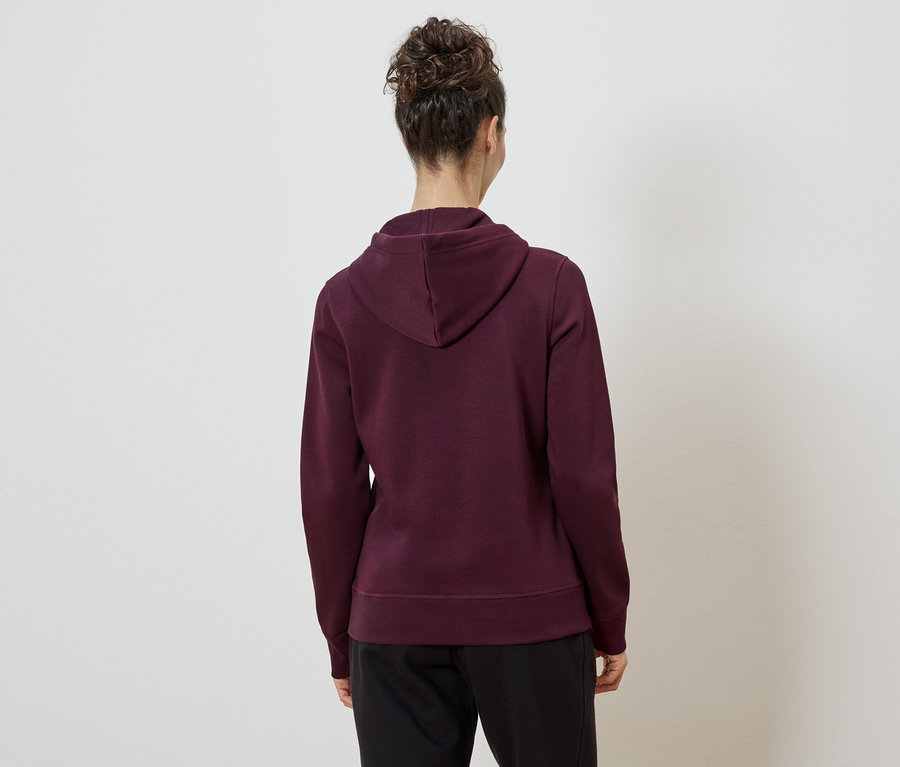 Rückansicht einer Frau mit Dutt, die einen bordeauxroten Kapuzenpullover und eine schwarze Hose vor einem weißen Hintergrund trägt.