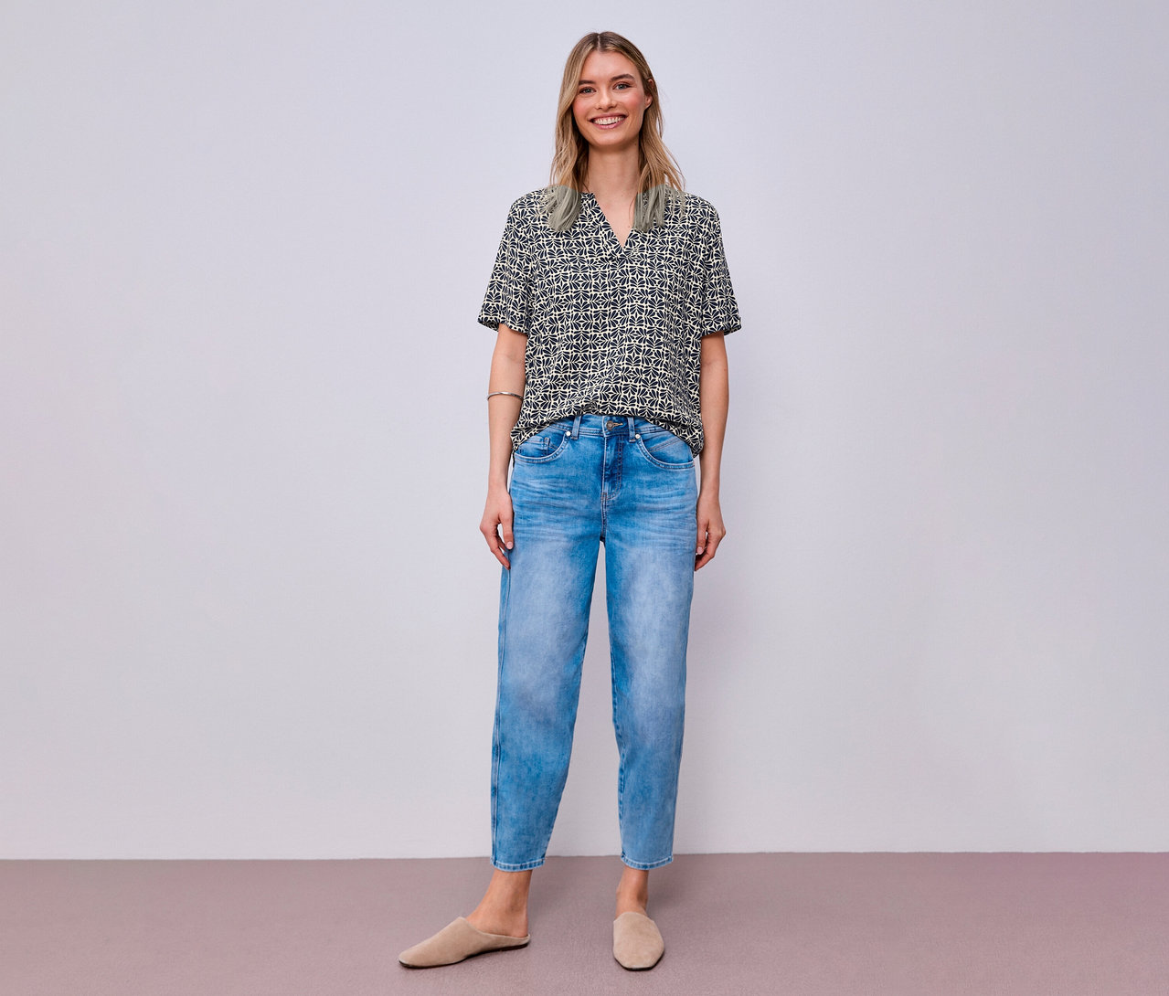 Frau in Jeans und Street One Webbluse mit Muster, dazu beigefarbene Slipper.