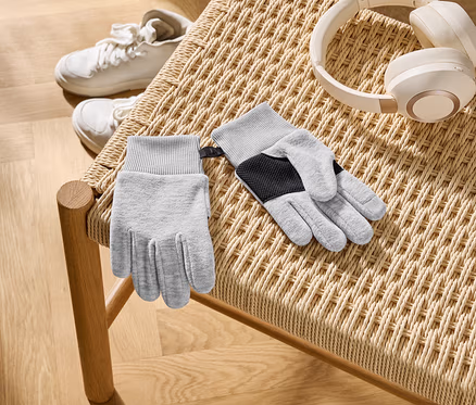 Auf einem geflochtenen Stuhl liegen graue Handschuhe, weiße Kopfhörer und weiße Turnschuhe.