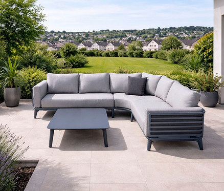 Anthrazitfarbene Leco Lounge-Ecke »Moss« mit Tisch auf einer Terrasse mit Blick auf einen Rasen und Häuser.