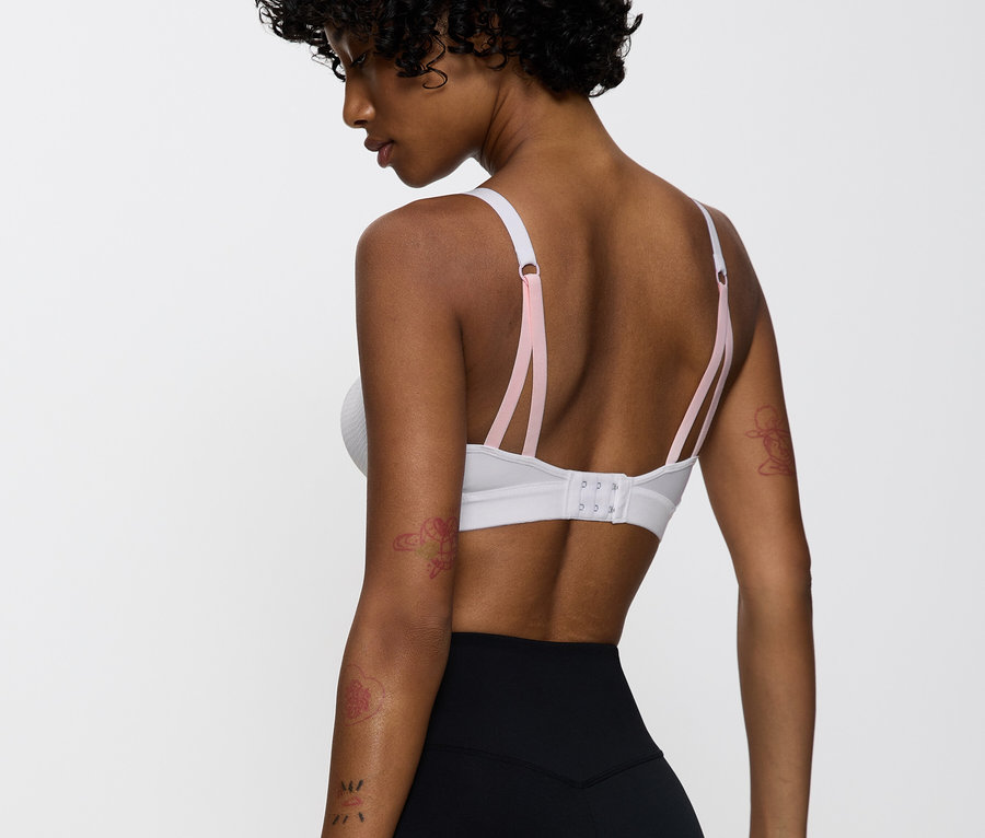 Frau trägt einen weißen Sport-BH mit rosa Trägern und eine schwarze Leggings.