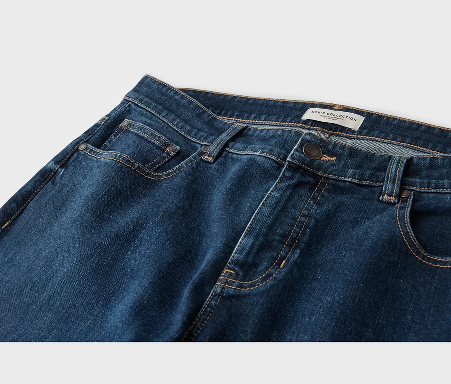 Nahaufnahme einer dunkelblauen Jeans mit hellbraunen Nähten, Metallknopf und Nieten. Ein "MEN'S COLLECTION"-Etikett ist am Bund sichtbar.