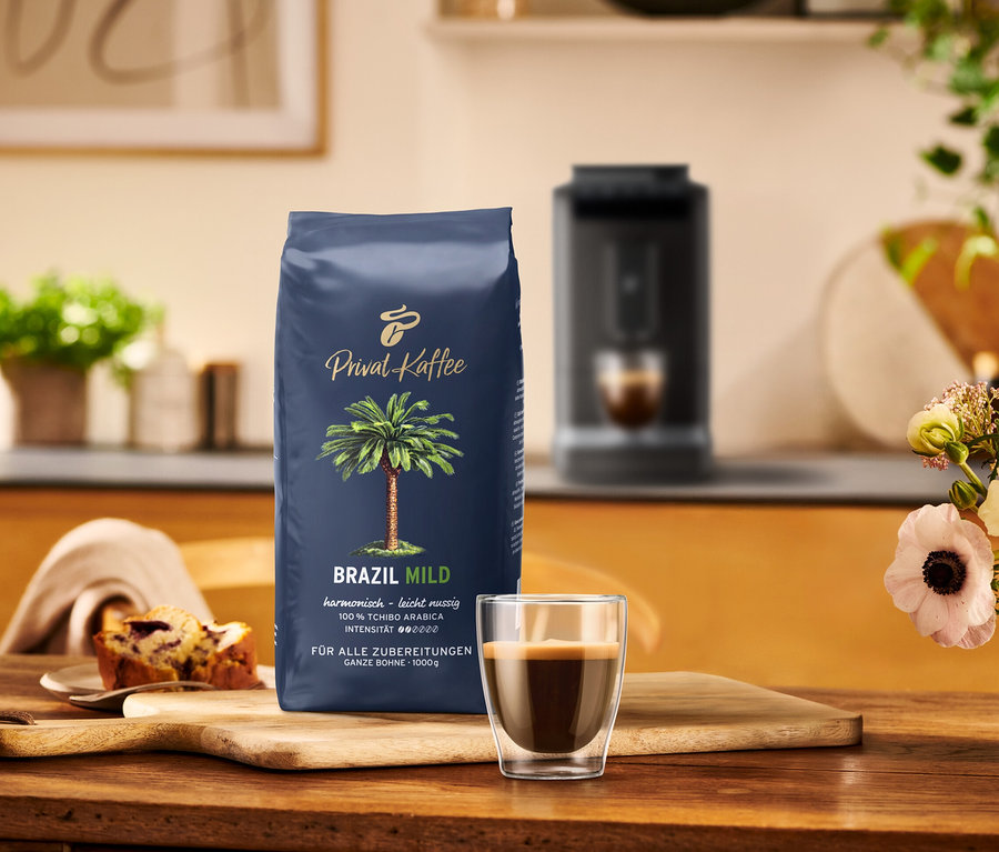 Eine Packung Tchibo Privat Kaffee Brazil Mild, eine Tasse Espresso und ein Stück Kuchen auf einem Holztisch.