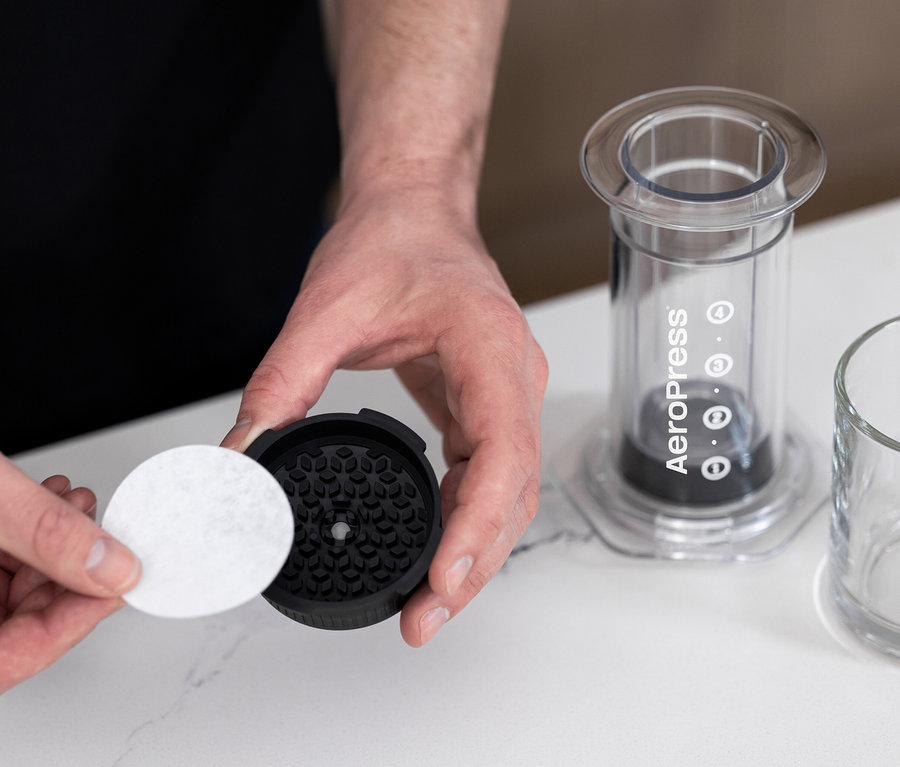 Mann setzt Papierfilter in einen transparenten AeroPress Coffee Maker »Clear« ein.